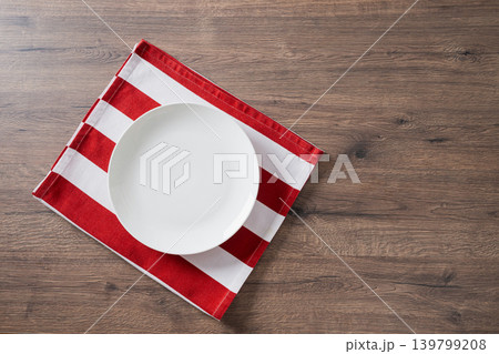 Empty white plate on red striped napkin over wooden table Empty white plate on red striped napkin over wooden table 139799208