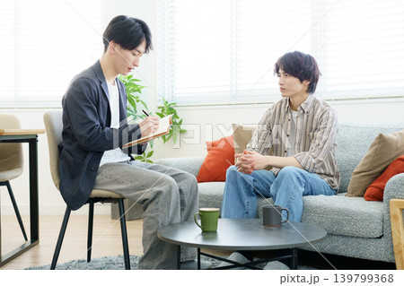 カウンセリング ソファに座って話をする若い日本人男性と話を聞きながらメモをする若い日本人医師 カウンセリング ソファに座って話をする若い日本人男性と話を聞きながらメモをする若い日本人医師 139799368
