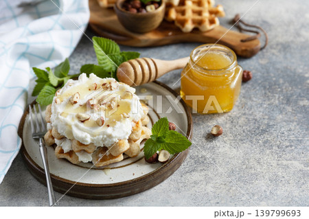 Belgian waffles with ricotta cheese, honey and hazelnuts for breakfast on a stone background. Sweet breakfast gluten free. Summer homemade recipe. Copy space. Belgian waffles with ricotta cheese, honey and hazelnuts for breakfast on a stone background. Sweet breakfast gluten free. Summer homemade recipe. Copy space. 139799693