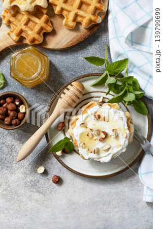 Belgian waffles with ricotta cheese, honey and hazelnuts for breakfast on a stone background. Sweet breakfast gluten free. Summer homemade recipe. View from above. Copy space. Belgian waffles with ricotta cheese, honey and hazelnuts for breakfast on a stone background. Sweet breakfast gluten free. Summer homemade recipe. View from above. Copy space. 139799699