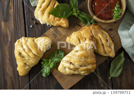 Mini savory meat pies from flaky dough on a wooden board over wooden background. View from above. Mini savory meat pies from flaky dough on a wooden board over wooden background. View from above. 139799751