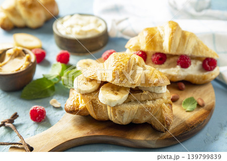 French pastry close up, freshly baked croissants with peanut butter, raspberries and banana on a blue stone background. Healthy food dessert concept. French pastry close up, freshly baked croissants with peanut butter, raspberries and banana on a blue stone background. Healthy food dessert concept. 139799839