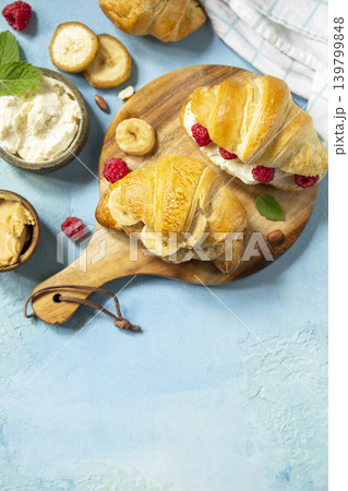French pastry, freshly baked croissants with peanut butter, raspberries and banana on a blue stone background. Healthy food dessert concept. View from above. Copy space. French pastry, freshly baked croissants with peanut butter, raspberries and banana on a blue stone background. Healthy food dessert concept. View from above. Copy space. 139799848