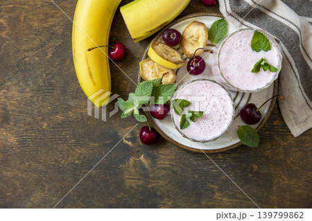 Pink cherries and banana fruit smoothie or milk protein shake on stone tabletop. Yogurt cocktail, natural detox. Liquid ice cream. View from above. Copy space. Pink cherries and banana fruit smoothie or milk protein shake on stone tabletop. Yogurt cocktail, natural detox. Liquid ice cream. View from above. Copy space. 139799862