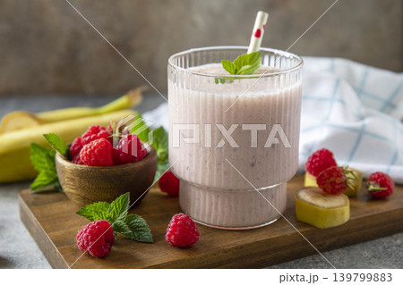 Pink raspberries and banana fruit smoothie or milk protein shake on stone tabletop. Yogurt cocktail, natural detox. Liquid ice cream. Pink raspberries and banana fruit smoothie or milk protein shake on stone tabletop. Yogurt cocktail, natural detox. Liquid ice cream. 139799883