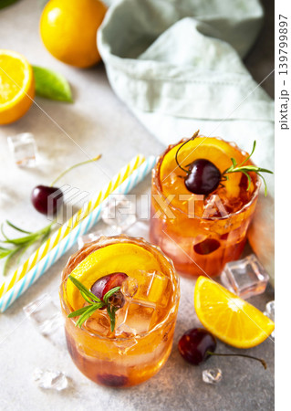 Refreshing summer cherry and orange cocktail cola lemonade or mojito cocktail in glass with ice and mint on stone tabletop. 139799897