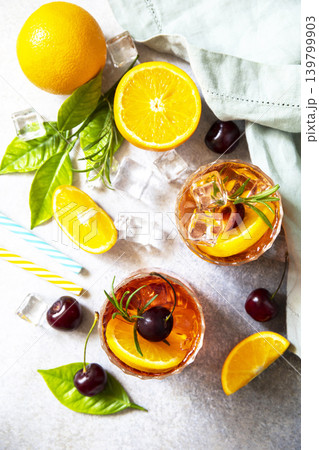 Refreshing summer cherry and orange cocktail cola lemonade or mojito cocktail in glass with ice and mint on stone tabletop. View from above. Refreshing summer cherry and orange cocktail cola lemonade or mojito cocktail in glass with ice and mint on stone tabletop. View from above. 139799903