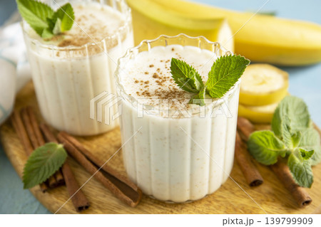 Vegan banana smoothie close up with cinnamon in drinking glass on a blue stone background. Detox menu, refreshing summer drink. Vegan banana smoothie close up with cinnamon in drinking glass on a blue stone background. Detox menu, refreshing summer drink. 139799909