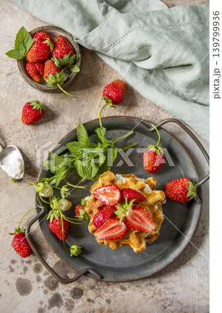 Belgian waffles with ricotta cheese and fresh strawberries for breakfast on a stone background. Sweet breakfast gluten free. Summer homemade recipe. View from above. Belgian waffles with ricotta cheese and fresh strawberries for breakfast on a stone background. Sweet breakfast gluten free. Summer homemade recipe. View from above. 139799936