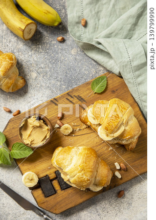 French pastry, freshly baked croissants with peanut butter and banana on a grey stone background. Healthy food dessert concept. View from above. 139799990