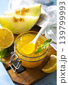 Sweet melon and citrus jam, homemade jelly preserves in small glass jar with fresh melon slices on a blue stone tabletop. Homemade preserve. 139799993