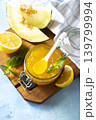 Sweet melon and citrus jam, homemade jelly preserves in small glass jar with fresh melon slices on a blue stone tabletop. Homemade preserve. Copy space. 139799994