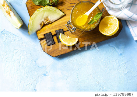 Sweet melon and citrus jam, homemade jelly preserves in small glass jar with fresh melon slices on a blue stone tabletop. Homemade preserve. View from above. Copy space. Sweet melon and citrus jam, homemade jelly preserves in small glass jar with fresh melon slices on a blue stone tabletop. Homemade preserve. View from above. Copy space. 139799997