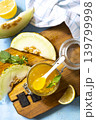 Sweet melon and citrus jam, homemade jelly preserves in small glass jar with fresh melon slices on a blue stone tabletop. Homemade preserve.  View from above. 139799998