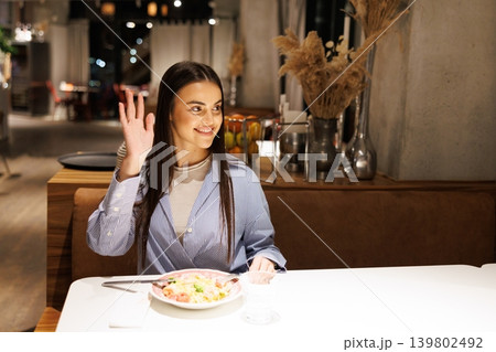 Young woman waving hand greeting at restaurant dinner Young woman waving hand greeting at restaurant dinner 139802492