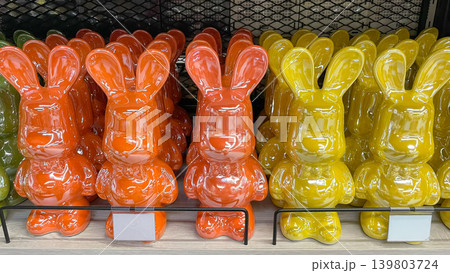 Bright orange and yellow glossy ceramic bunny figurines standing in rows on a modern retail shelf 139803724