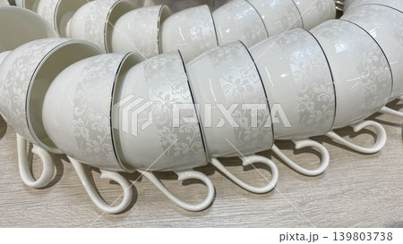 Elegant white porcelain tea cups with delicate floral patterns and gold rims on a store display shelf Elegant white porcelain tea cups with delicate floral patterns and gold rims on a store display shelf 139803738