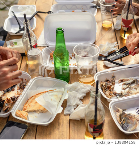 Used takeaway food containers, empty bottles, leftovers are scattered on wooden table after an outdoor meal. Concept of waste, pollution, environmental, disposable packaging, single use plastic waste Used takeaway food containers, empty bottles, leftovers are scattered on wooden table after an outdoor meal. Concept of waste, pollution, environmental, disposable packaging, single use plastic waste 139804159