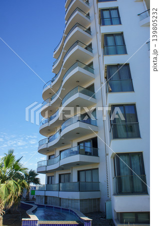 Elegant coastal apartment building with unique balconies overlooking a sunny blue sky and tranquil pool. Elegant coastal apartment building with unique balconies overlooking a sunny blue sky and tranquil pool. 139805232