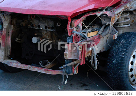Red car with missing front part shows signs of damage in parking lot during daylight Red car with missing front part shows signs of damage in parking lot during daylight 139805618