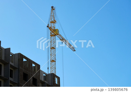 Two large cranes stand tall against the blue sky. They are positioned at a construction site Two large cranes stand tall against the blue sky. They are positioned at a construction site 139805676