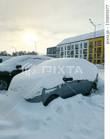 Snow covers the roofs and windshields of parked cars in a residential area. The sun sets in the background Snow covers the roofs and windshields of parked cars in a residential area. The sun sets in the background 139805677
