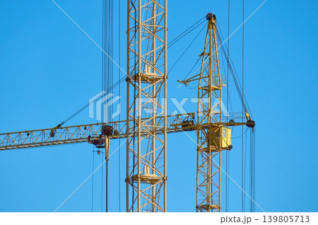 Cranes are lifting materials at a construction site in the city. The building work is ongoing under bright blue skies Cranes are lifting materials at a construction site in the city. The building work is ongoing under bright blue skies 139805713