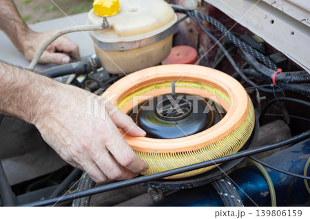 Mechanic changing air filter in an old car engine Mechanic changing air filter in an old car engine 139806159