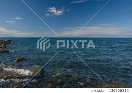 Tranquil seascape with gentle waves caressing rocky shore under a vast blue sky during midday 139806316