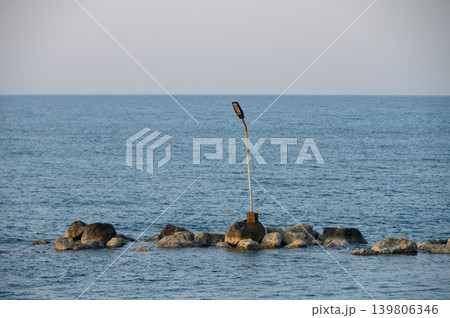 Lonely streetlight standing guard over calm ocean waves at dusk Lonely streetlight standing guard over calm ocean waves at dusk 139806346