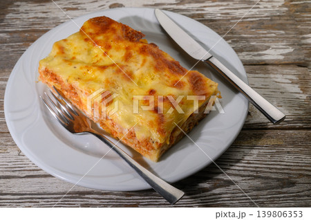 Deliciously baked lasagna resting on a rustic wooden table, perfectly prepared and ready to be enjoyed at a cozy Italian restaurant 139806353