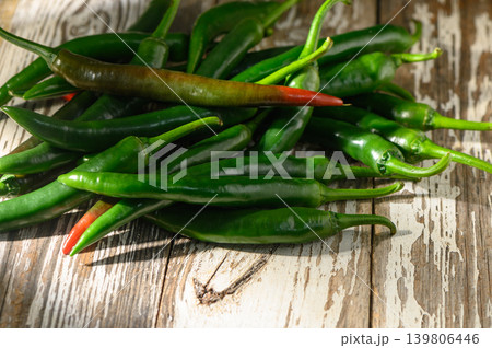 Fresh green chilies piled on rustic wooden surface in warm sunlight highlighting their vibrant colors Fresh green chilies piled on rustic wooden surface in warm sunlight highlighting their vibrant colors 139806446