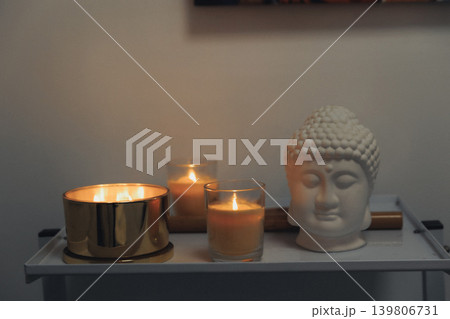 Candles glow warmly beside a serene Buddha head Candles glow warmly beside a serene Buddha head 139806731