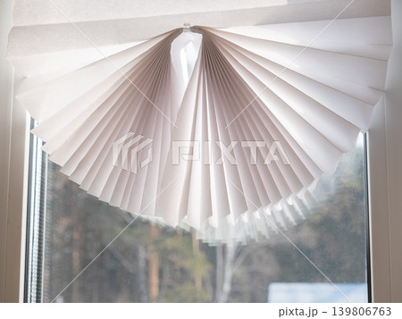 White pleated blind partially covering a window. Modern interior design element for home or office decor. Sun protection and privacy concept. 139806763