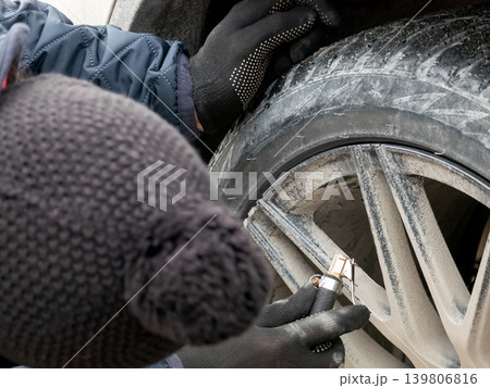 Man in gloves checking air pressure of winter car tire. Auto service concept for seasonal vehicle maintenance and safety control. 139806816