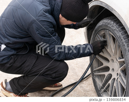 Man filling air in car tire with pump hose. Vehicle maintenance and safety. Automotive care and roadside assistance concept. 139806834
