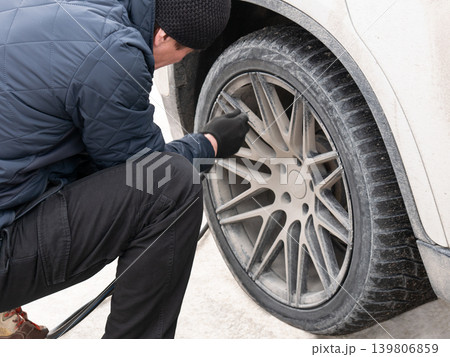 Man checking tire pressure on dirty car wheel. Driver maintaining car at gas station. Transportation and vehicle service concept. 139806859