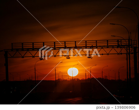 Dramatic red sunset sky silhouetting a road infrastructure and streetlights, evoking a serene and calm evening mood over the city. Dramatic red sunset sky silhouetting a road infrastructure and streetlights, evoking a serene and calm evening mood over the city. 139806906