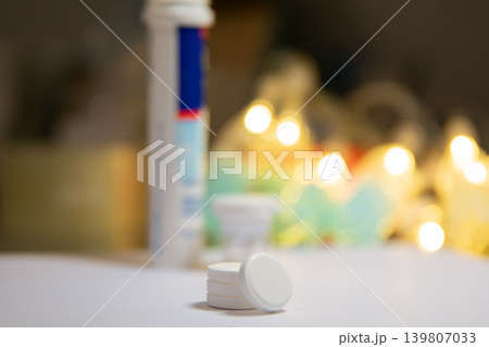 Effervescent tablet on table with tube in blurred background. Medical pill for health treatment and vitamin supplement. Nutritional care and pharmacy product for wellness daily routine. 139807033