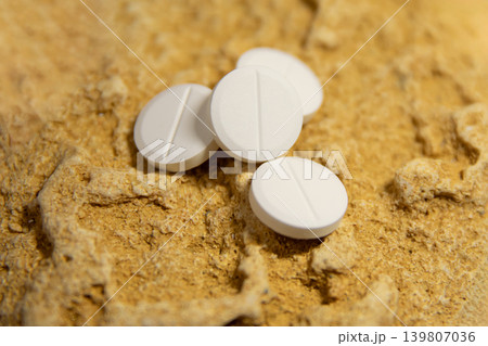 White pills on textured stone surface. Medicinal tablet supplement for healthcare treatment. Pharmaceutical product for chemical therapy and pain relief. Medical science and health concept. White pills on textured stone surface. Medicinal tablet supplement for healthcare treatment. Pharmaceutical product for chemical therapy and pain relief. Medical science and health concept. 139807036