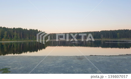 Calm lake with pine forest reflection at sunset. Serene natural landscape with clear sky and forest belt. Scenic outdoor environment for relaxation, travel, tourism and wilderness. Calm lake with pine forest reflection at sunset. Serene natural landscape with clear sky and forest belt. Scenic outdoor environment for relaxation, travel, tourism and wilderness. 139807057