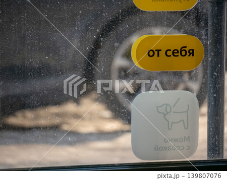 Yellow sign saying pull to open (?? ????) on a dirty window with a dog allowed sticker. Concept of entrance and exit during winter. 139807076