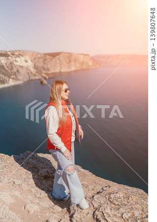 Woman cliff sea standing on a high rocky edge overlooking the blue ocean during a bright sunny day Woman cliff sea standing on a high rocky edge overlooking the blue ocean during a bright sunny day 139807648