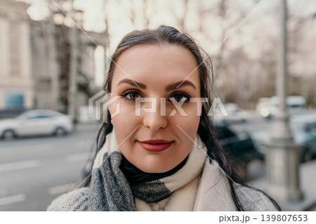 Woman portrait scarf Close-up portrait of a young woman with red lipstick wearing a warm plaid scarf on a city street during winter Woman portrait scarf Close-up portrait of a young woman with red lipstick wearing a warm plaid scarf on a city street during winter 139807653