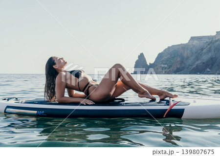 Woman Paddleboard Ocean - Relaxing on paddleboard in ocean, enjoying the sun and the view of the coastline. 139807675