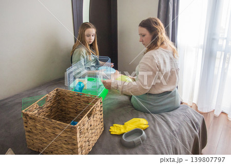 woman an girl sit on a bed in a room. Mom is holding a green hamster house with hamster woman an girl sit on a bed in a room. Mom is holding a green hamster house with hamster 139807797
