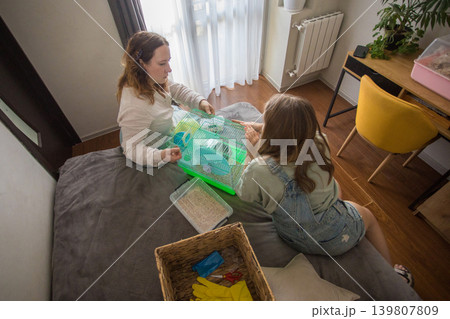 young girl and an adult are in a bedroom preparing a hamster cage. young girl and an adult are in a bedroom preparing a hamster cage. 139807809