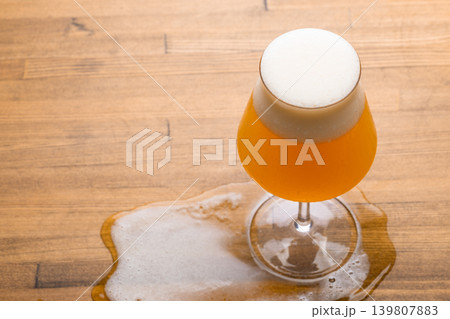 Foamy beer glass with spill on wooden table Foamy beer glass with spill on wooden table 139807883