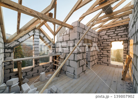 House interior under construction and renovation. Energy saving walls of hollow foam insulation blocks and bricks, ceiling beams and roof frame. House interior under construction and renovation. Energy saving walls of hollow foam insulation blocks and bricks, ceiling beams and roof frame. 139807902