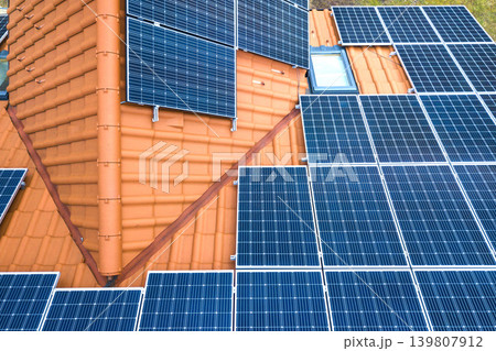 Aerial top view of new modern residential house cottage with blue shiny solar photo voltaic panels system on roof. Renewable ecological green energy production concept. Aerial top view of new modern residential house cottage with blue shiny solar photo voltaic panels system on roof. Renewable ecological green energy production concept. 139807912